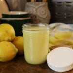 Jar of homemade lemon syrup for pancakes with fresh lemons on a wooden countertop.