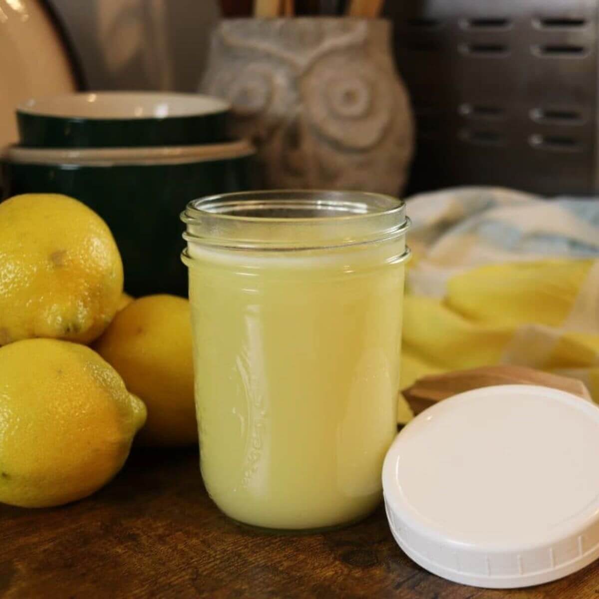 Jar of homemade lemon syrup for pancakes with fresh lemons on a wooden countertop.