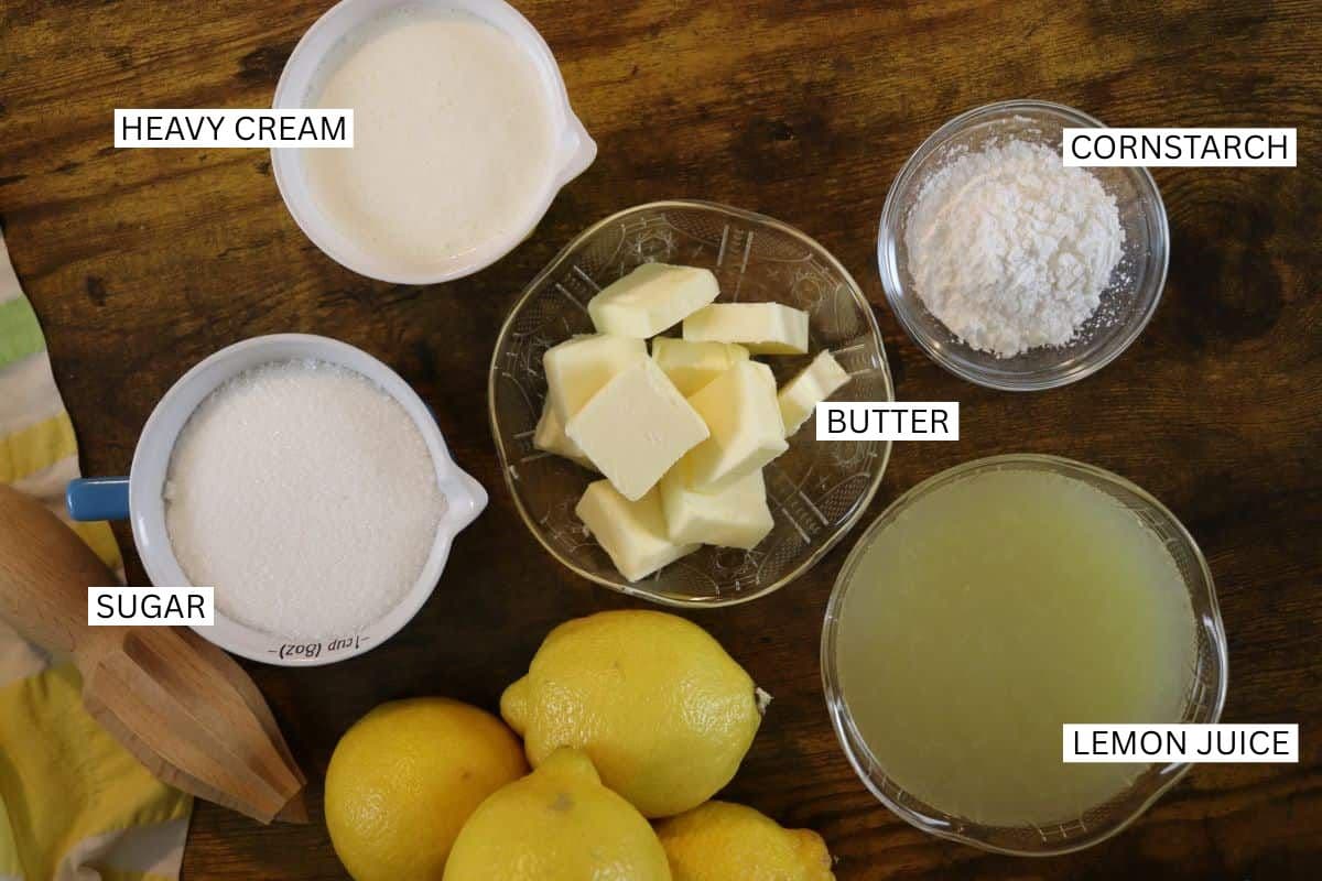 Labeled ingredients on a wooden surface: heavy cream, cornstarch, butter, sugar, lemon juice, and whole lemons.