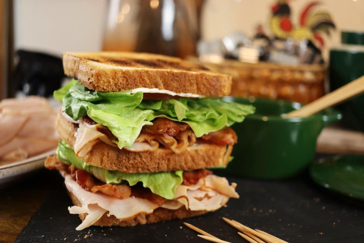 double decker sandwich on toast with each layer made of turkey, bacon, tomato, and lettuce.