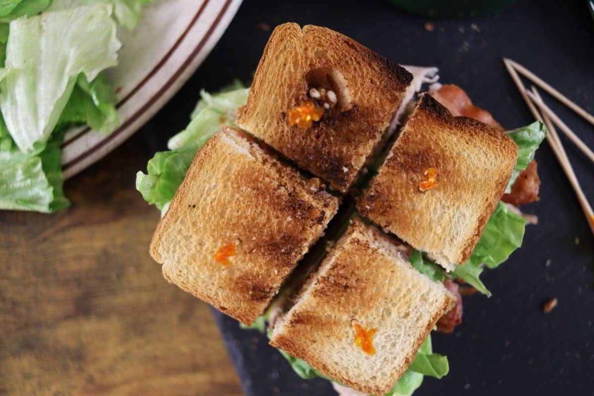 a sandwich made with toast cut in four pieces with each piece held together by a frilled club pick.