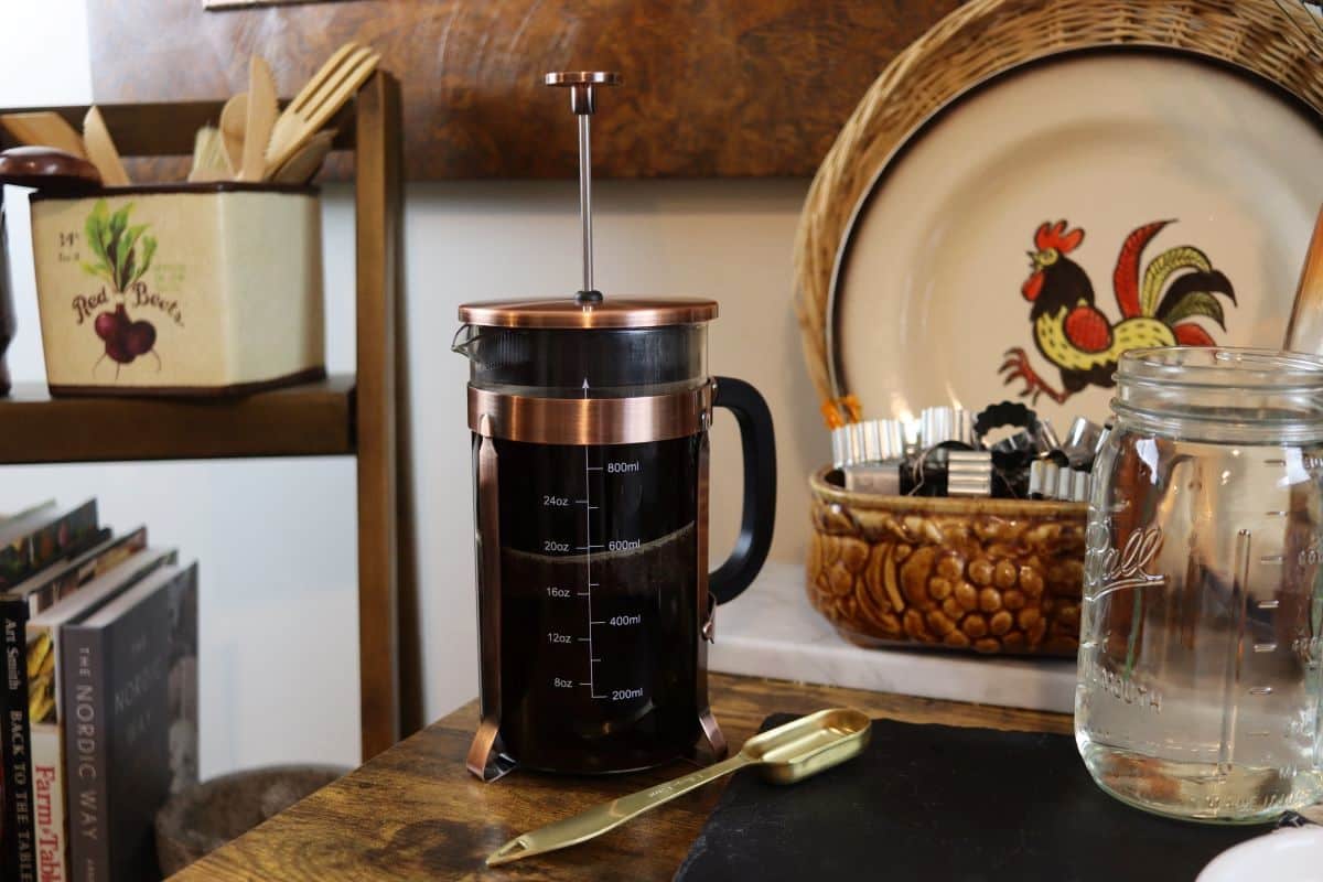 french press coffee maker full of grounds and water with the plunger submerged halfway sitting on a counter.