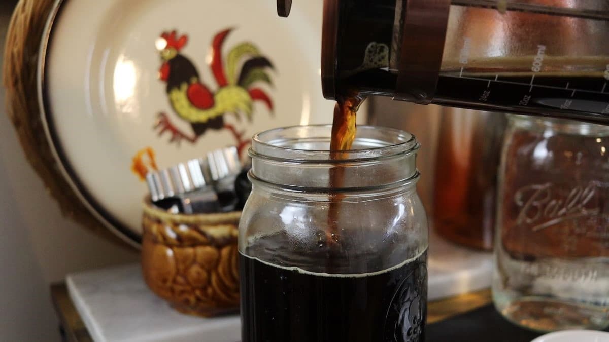 pouring fresh brewed coffee from a french press into a mason jar.