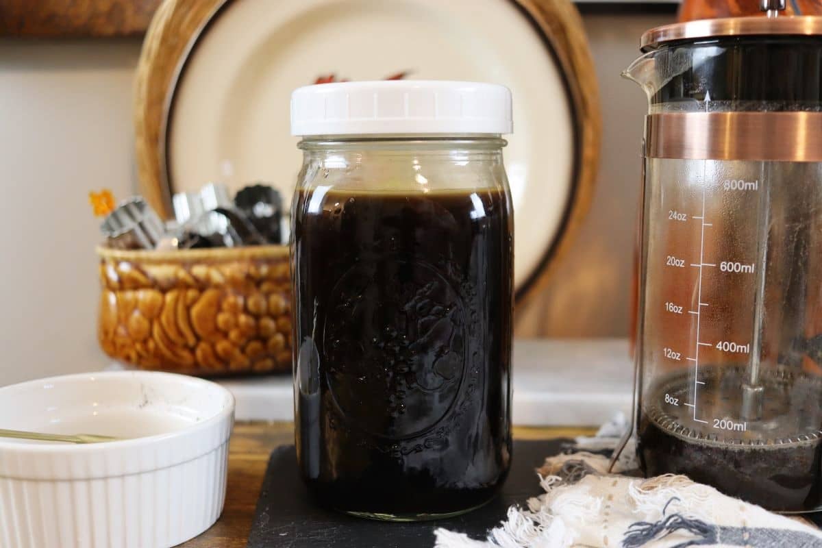 mason jar full of black coffee on a table next to an empty french press.