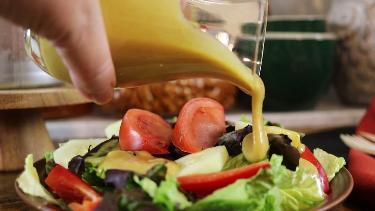 pouring yellow dressing over a small garden salad from a serving carafe.