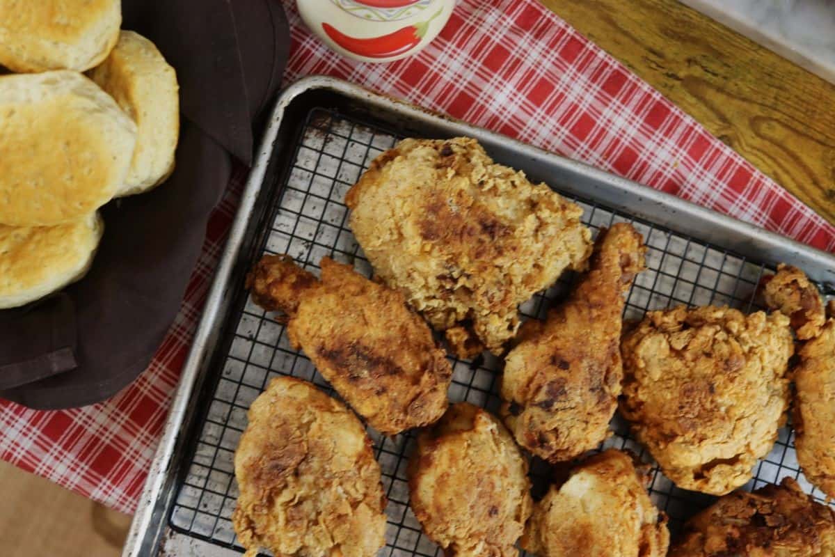 Pieces of breaded fried chicken sitting on a wire rack in a sheet pan on top of a red checkered cloth.