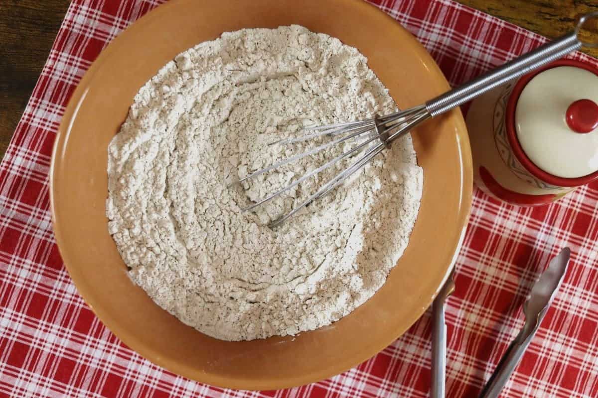 Flour mixture in a bowl with a whisk in it sitting on a red checkered cloth.