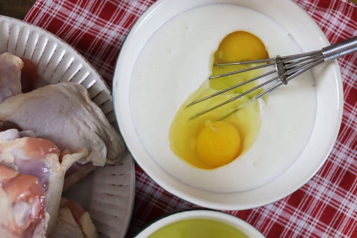 Buttermilk and eggs in a bowl with a whisk in it sitting on a red checkered cloth.