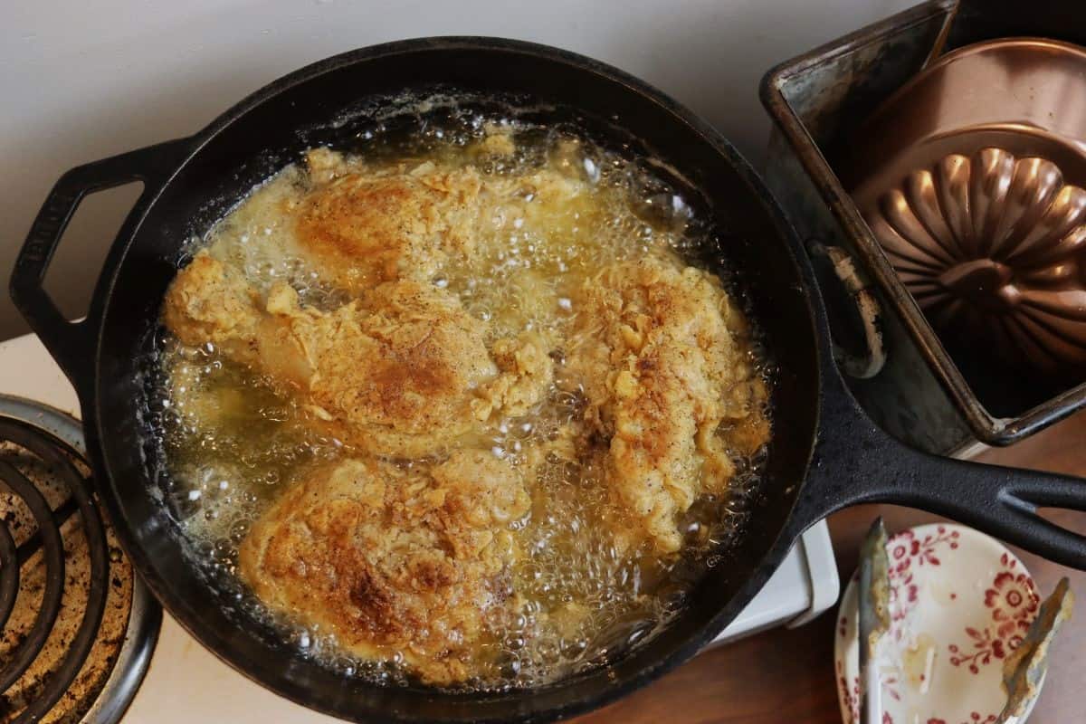 Pieces of breaded chicken frying in a cast iron skillet of oil.