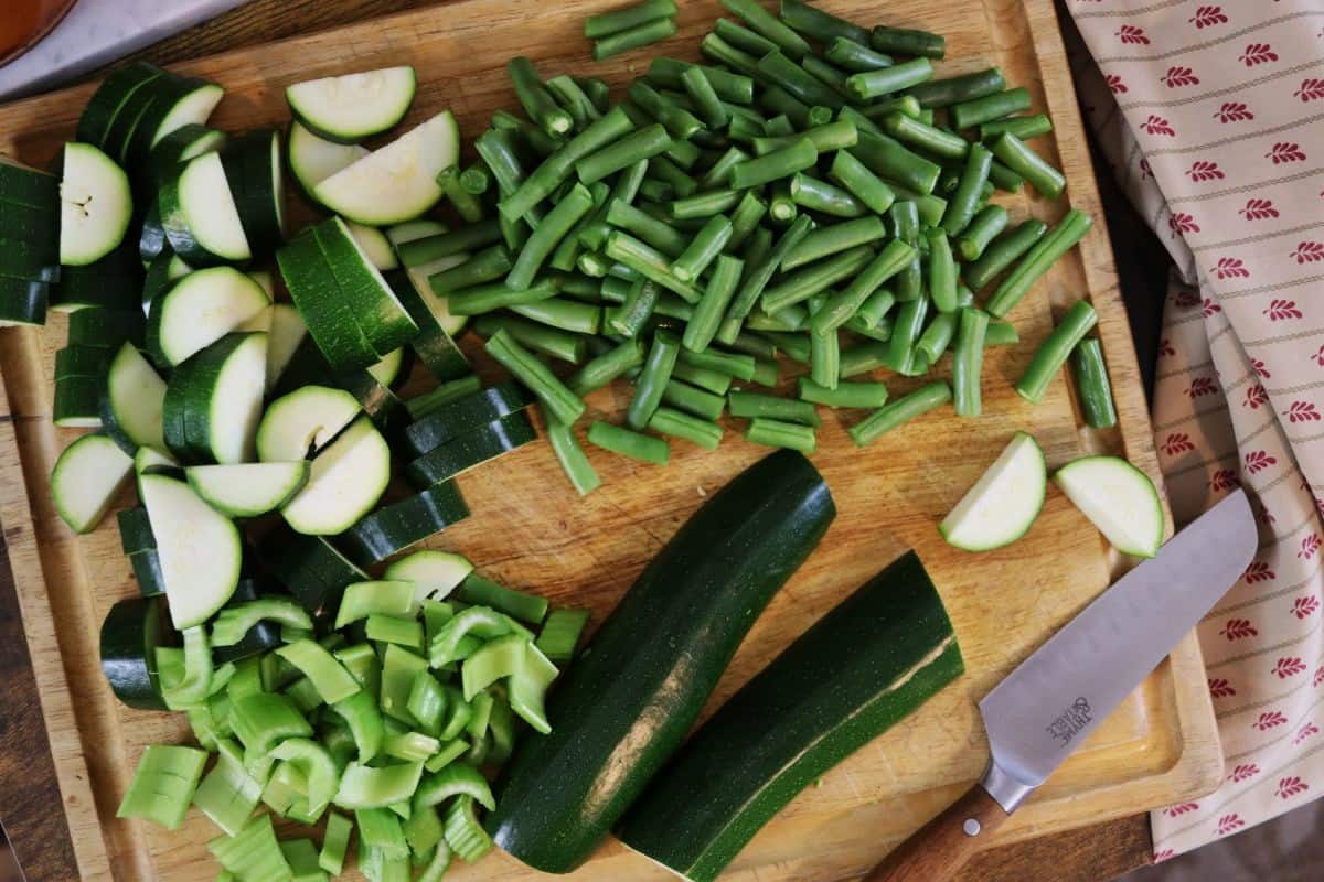 chopped zucchini, string beans, and celery sitting on a cutting board with a knife on it.