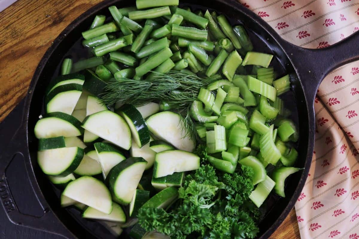 cast iron dutch oven skillet full of cut up zucchini, celery, string beans, and fresh parsley and dill.