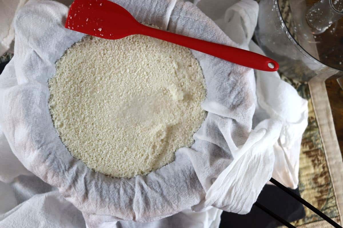 almond pulp straining through a flour sack towel with a spatula.