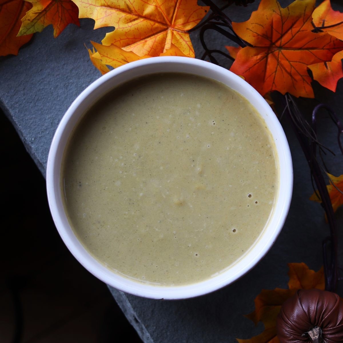 overview of a bowl of green soup on a stone slab with autumn leaves next to it.