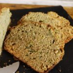 Three slices of amish zucchini bread on a slate board with the tip of a bread knife visible in front of them.