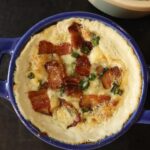 Small blue crock full of white dip topped with bacon pieces and scallions.