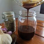 pouring balsamic mustard dressing from a bowl into a mason jar.