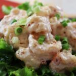 Shrimp covered in a creamy white sauce and topped with chopped scallions, with red pepper flakes on them, sitting on a bed of lettuce.