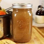 Mason jar of beef broth on a cutting board with a pot visible in the background.