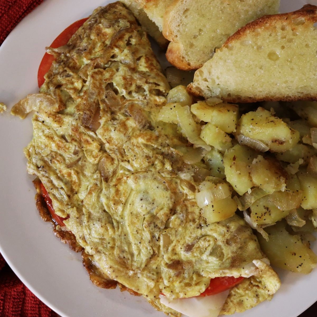 overview of an omelet on a plate with homefries and toast.