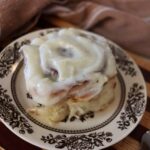 Cinnamon roll topped with white icing sitting on a small brown and white dish.
