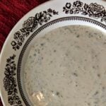 white dressing with herbs in it in a dish on a table next to a red cloth.