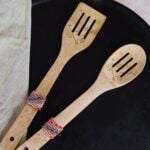 two wooden spoons with a beaded band around the bottom of the handle laying on a table.