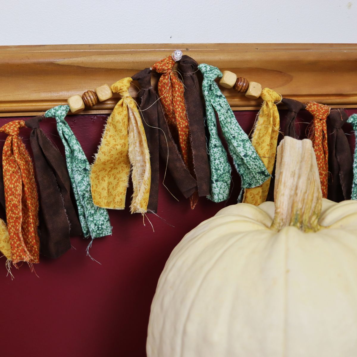 Fall rag tie garland with beads handing on the wall behind a white pumpkin.
