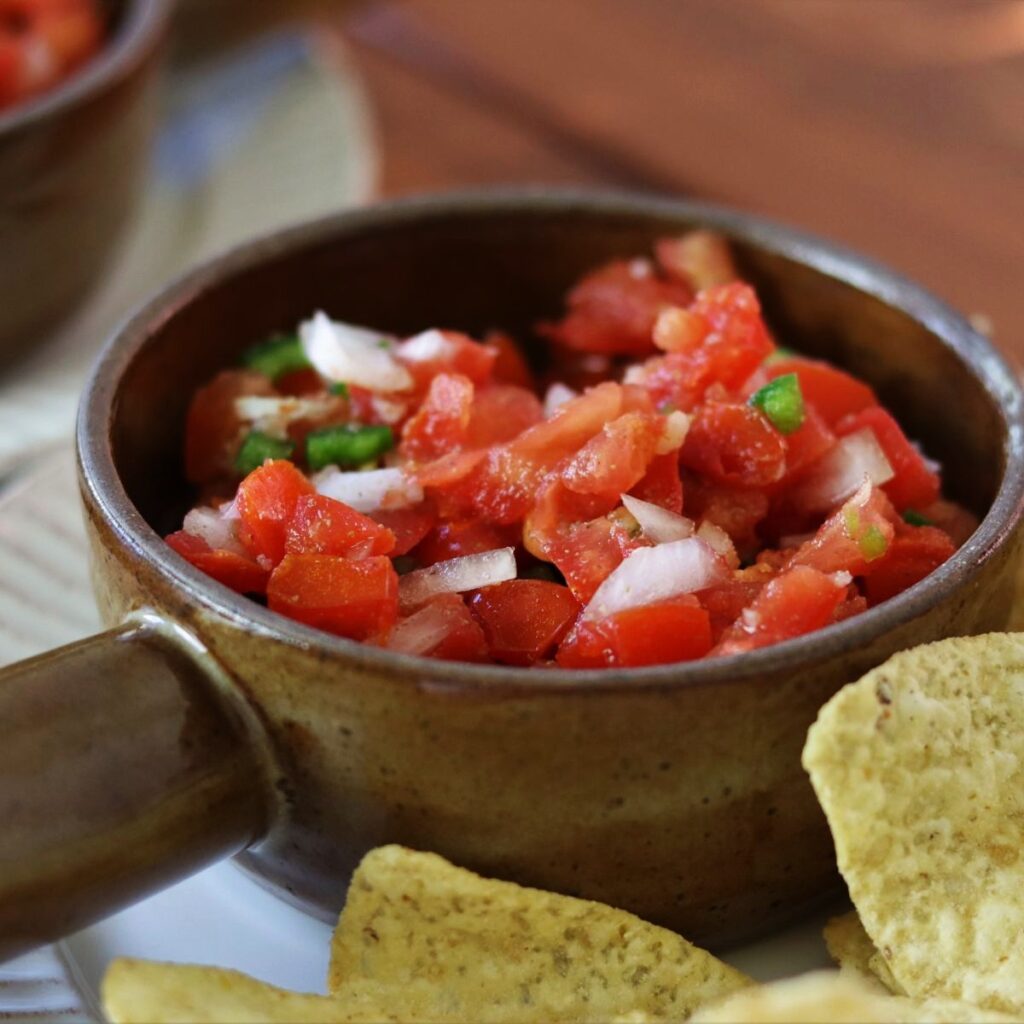 garden fresh pico de gallo in a serving bowl on a plate with tortilla chips.