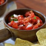 Diced tomatoes, onions, and jalapeno in a small crock with tortilla chips on the side.