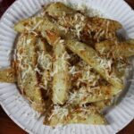 Fried potato wedges sprinkled with asiago cheese and spices on a white dish.
