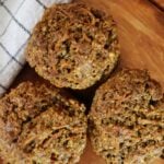 Three muffins sitting in a triangle on a wooden surface with a green and white cloth next to them.