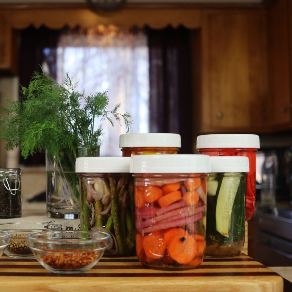 mason jars of vegetables sitting on a counter with condiment dishes and a bouquet of dill.