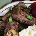Slices of cooked beef topped with scallions and mashed potatoes visible on the edge of the image.