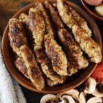 Cooked sausage links piled on a plate with sliced mushrooms visible to the side.