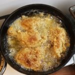 Breaded chicken frying in a cast iron skillet full of oil.