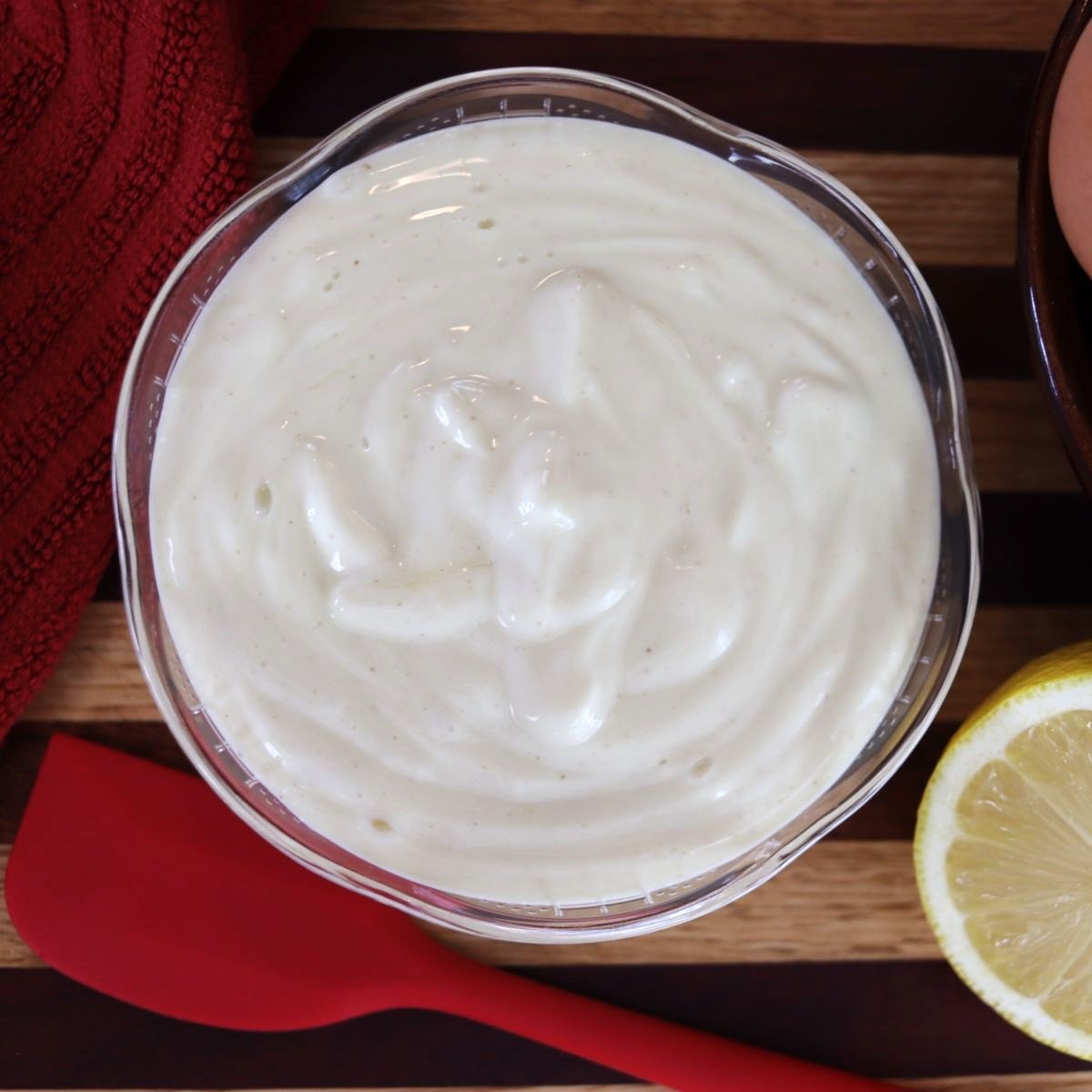 overview of a small dish of homemade mayonnaise witha spatula and a lemon next to it.