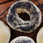 Poppy seed bagel on a cooling rack with the edge of other bagels visible at the bottom of the image.