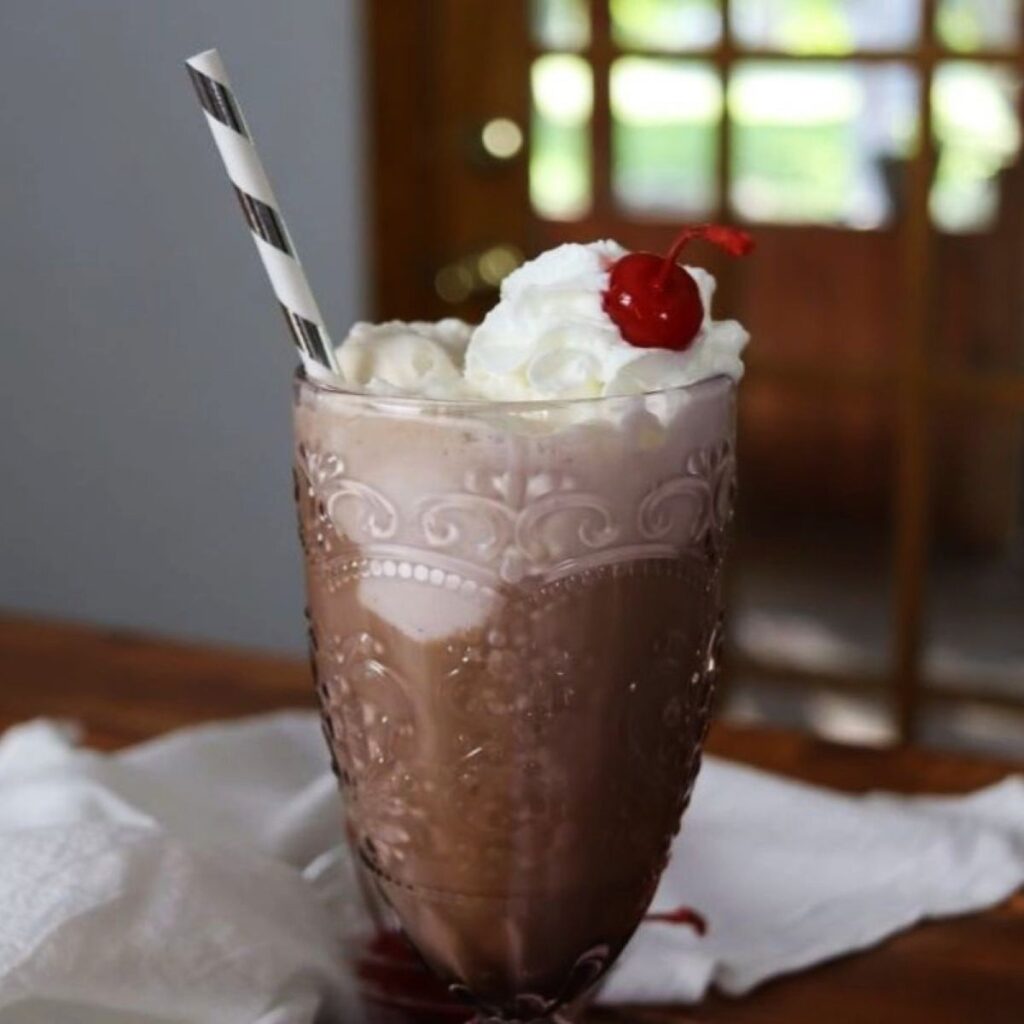 soda fountain glass with beverage in it, topped with whipped cream and a cherry.