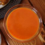 Small condiment dish of orange sauce on a wooden tabletop.