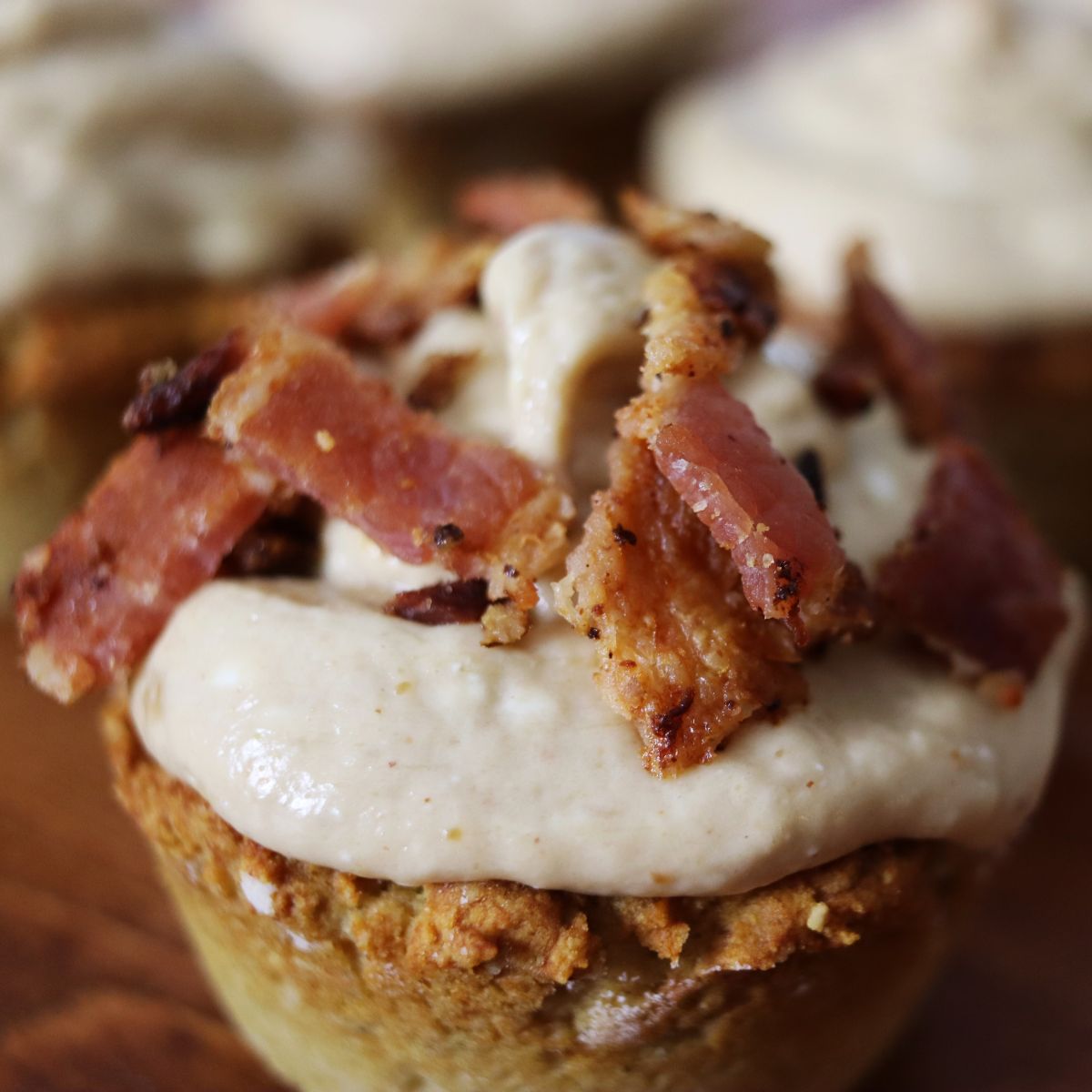 Muffin shaped dog treat with a light brown base, creamy topping and chopped bacon.