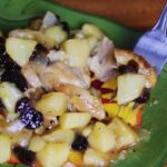 A forkful of pear raisin chutney being lifted from a plate of it on top of chicken.