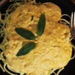 Linguine pasta topped with orange sauce and three fresh sage leaves on a black plate.