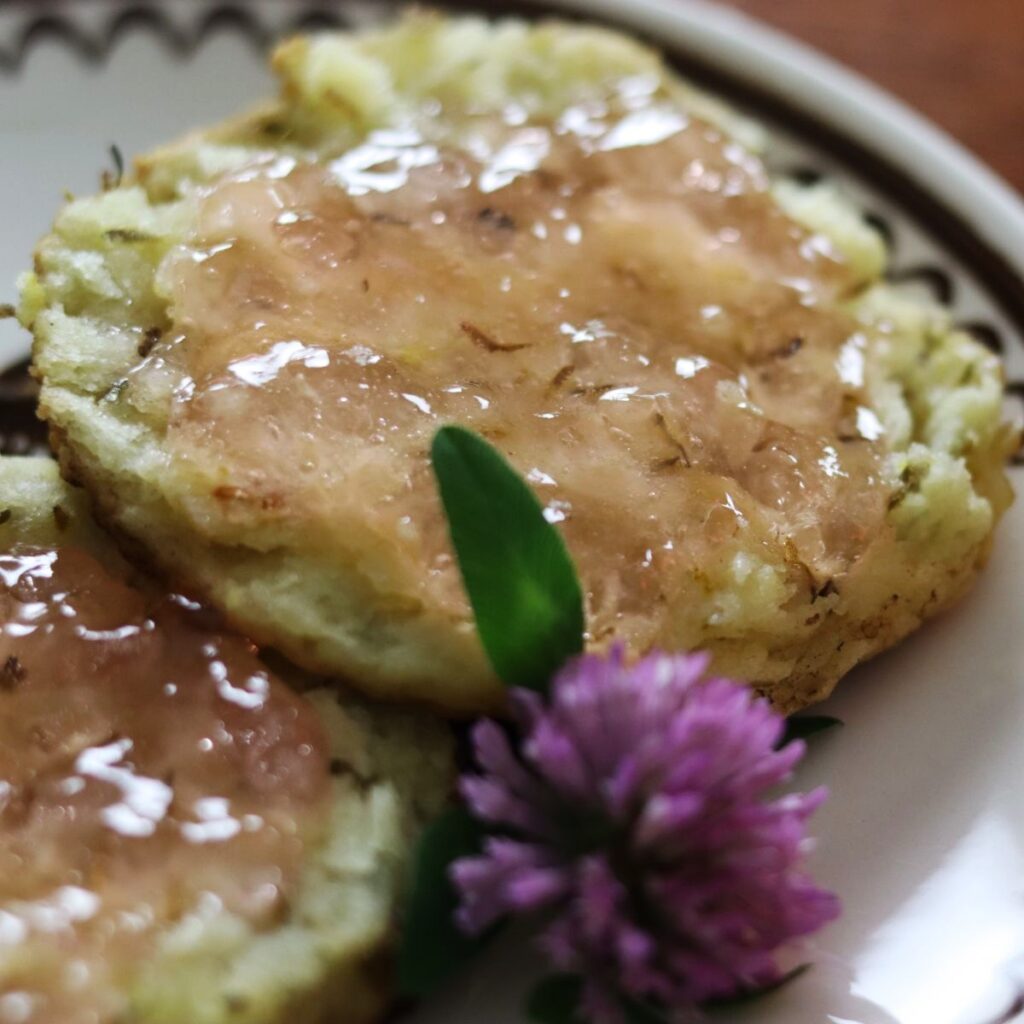 english muffin covered in jelly on a small plate with a red clover garnish.