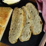 Three slices of bread cut from a loaf on a dark slate board.