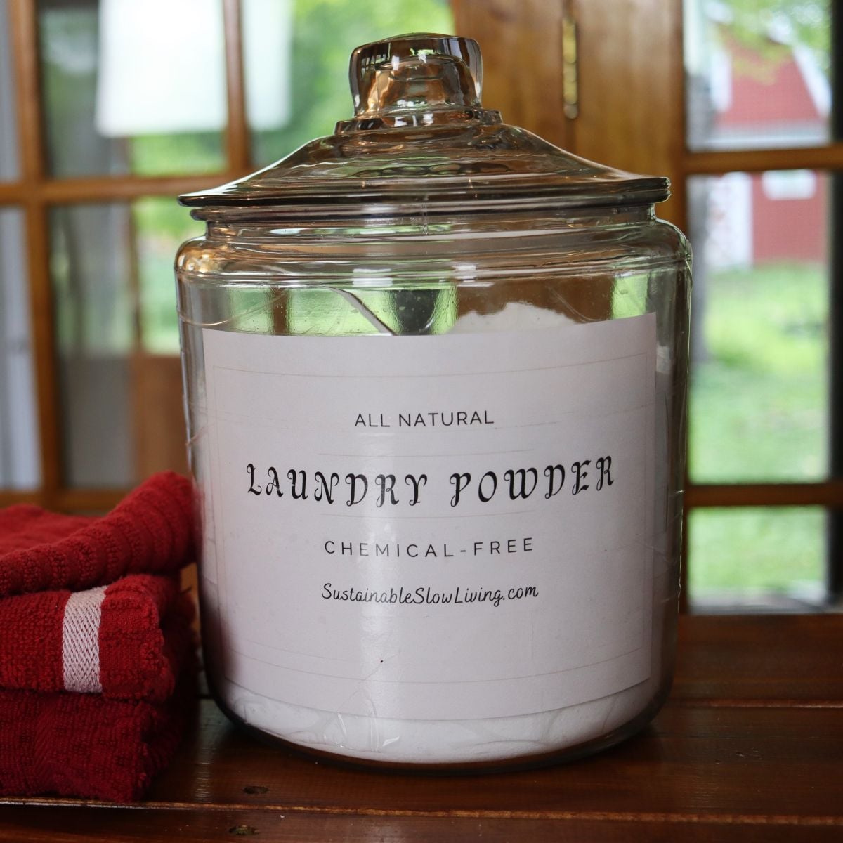 Large glass jar full of laundry powder with label sitting on a table next to towels.