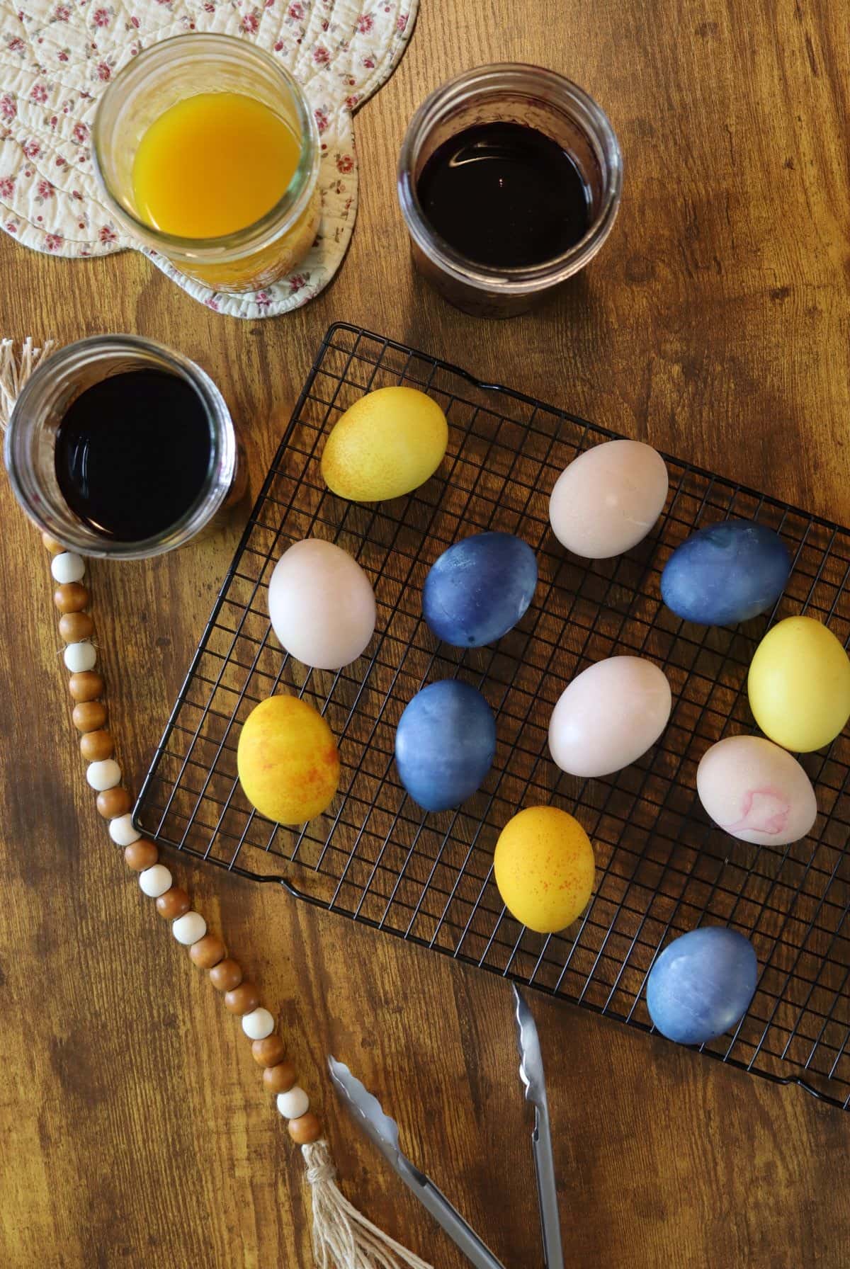colored eggs on a cooling rack with mason jars of natural dye next to them.