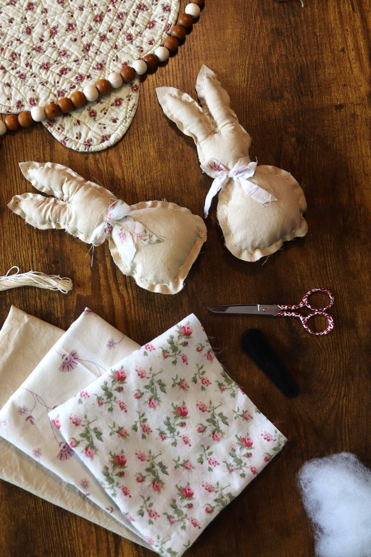 two handmade stuffed bunnies on a table with scissors, thread, and fabric.