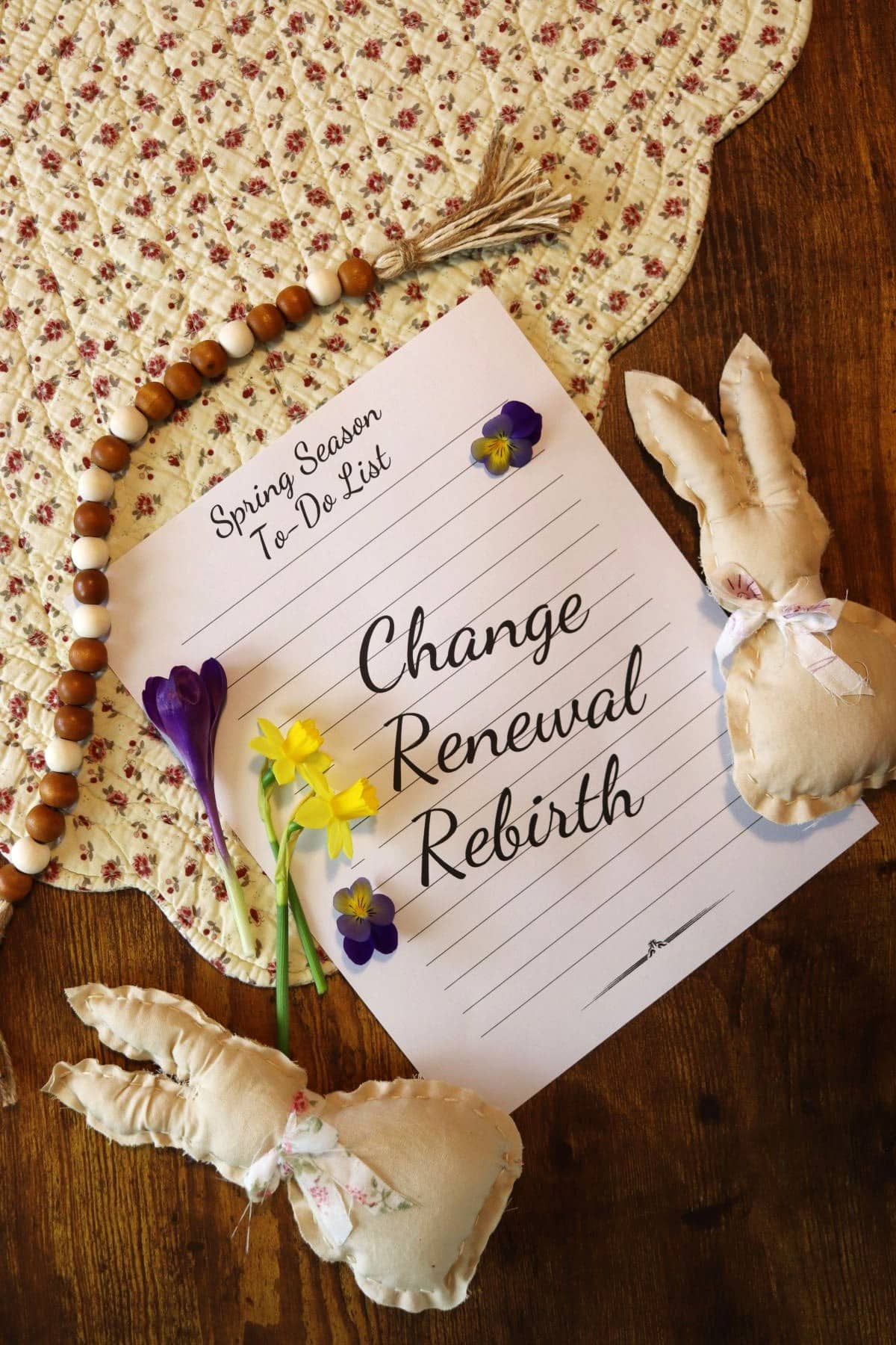 spring season to do list on a table with daffodil and crocus stems, a sting of wooden beads, and handmade rustic fabric bunnies.