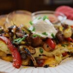 Big, fluffy omelet on a plate with cheese visible on the inside and red bell pepper strips, onion strips, steak strips, and a small scoop of sour cream on top.