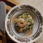 Portobello mushroom full of stuffing with a shrimp on top in a small brown and white bowl.